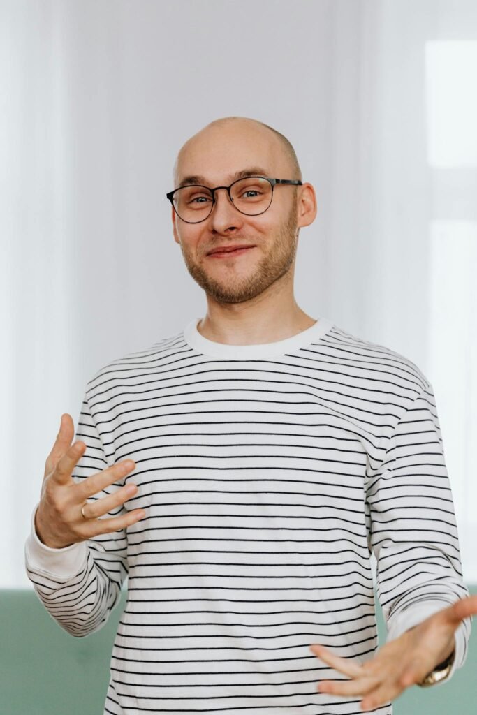 Casual portrait of a smiling bald man with a beard and glasses in a striped shirt indoors.